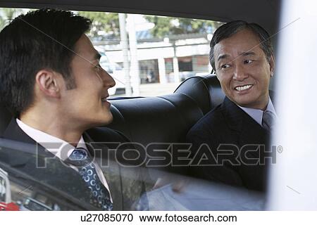Stock Image - Businessmen riding together in taxi. Fotosearch