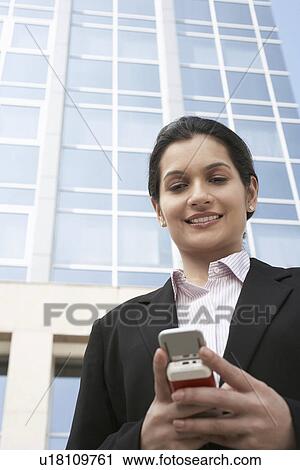 Stock Image - Businesswoman using cell phone outdoors. Fotosearch