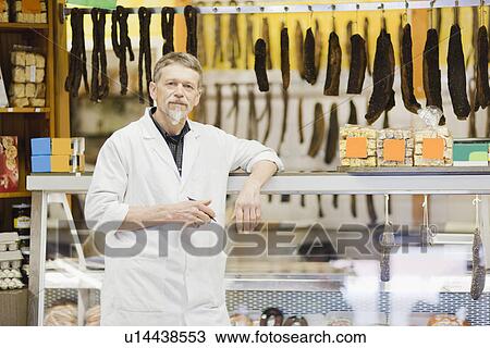 Stock Image - Butcher standing at meat counter. Fotosearch