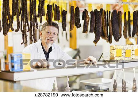 Stock Image - Butcher standing at meat counter. Fotosearch