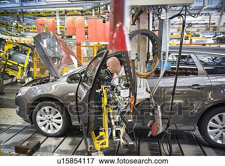 Stock Photo - Car assembly workers fitting doors to cars on production line in car factory. Fotosearch