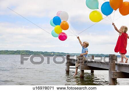 Children holding balloons on wooden pier View Large Photo Image Stock Image - Children holding balloons on wooden pier. Fotosearch