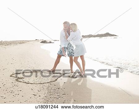 Couple drawing heart in sand on beach View Large Photo Image Picture - Couple drawing heart in sand on beach. Fotosearch