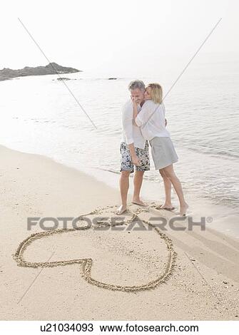 Couple drawing heart in sand on beach View Large Photo Image Stock Image - Couple drawing heart in sand on beach. Fotosearch