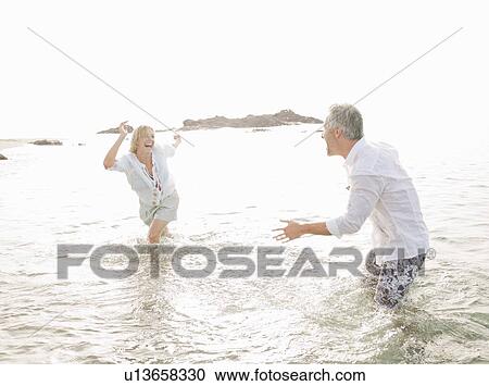 Couple playing in waves on beach View Large Photo Image Stock Image - Couple playing in waves on beach. Fotosearch