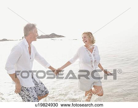Stock Image - Couple playing in waves on beach. Fotosearch