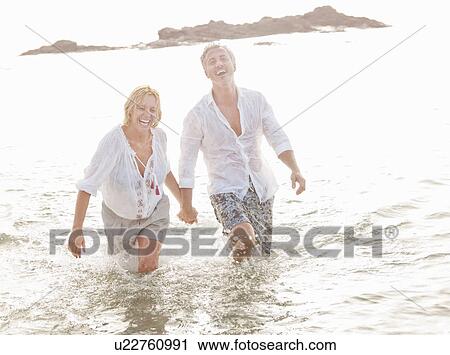 Stock Image - Couple playing in waves on beach. Fotosearch