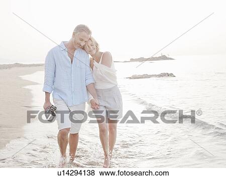 Stock Photo - Couple walking in waves on beach. Fotosearch