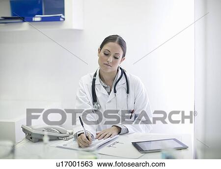 Stock Image - Doctor writing notes at desk. Fotosearch
