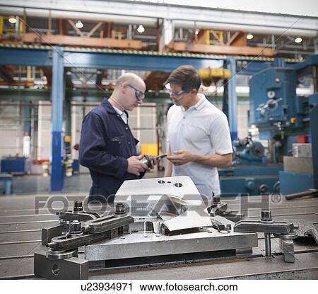 Stock Image - Engineers discussing car parts in car factory. Fotosearch