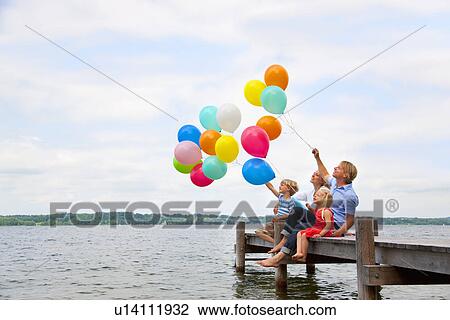 Stock Image - Family holding balloons on wooden pier. Fotosearch