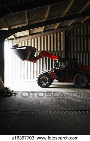 Stock Image - Farmer driving digger in shed. Fotosearch