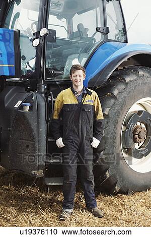 Stock Image - Farmer standing by tractor in field. Fotosearch