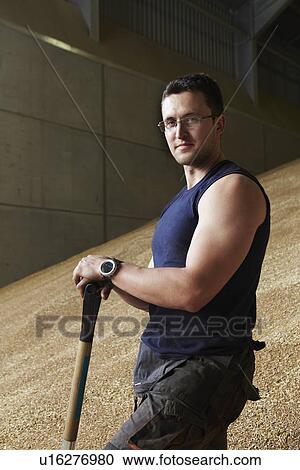 Stock Image - Farmer standing in shed of grain. Fotosearch
