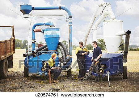 Stock Image - Farmers talking by machinery in field. Fotosearch