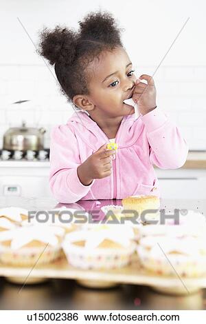 Girl eating cupcake frosting in kitchen View Large Photo Image Stock Photograph - Girl eating cupcake frosting in kitchen. Fotosearch