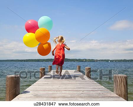 Stock Photo - Girl holding balloons on wooden pier. Fotosearch
