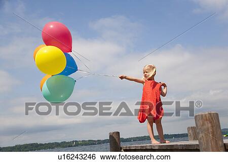 Stock Photograph - Girl holding balloons on wooden pier. Fotosearch