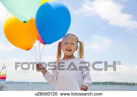 Stock Image - Girl holding bunch of balloons outdoors. Fotosearch
