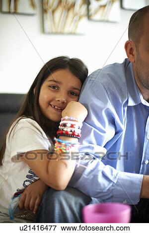 Stock Photo - Girl hugging fathers arm on sofa. Fotosearch