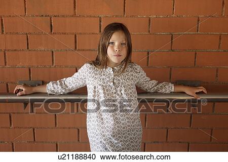 Stock Image - Girl leaning on banister on brick wall. Fotosearch