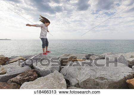 Stock Image - Girl playing on rocks at beach. Fotosearch