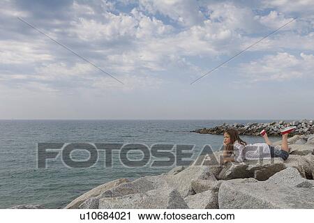 Girl relaxing on rocky beach View Large Photo Image Stock Image - Girl relaxing on rocky beach. Fotosearch
