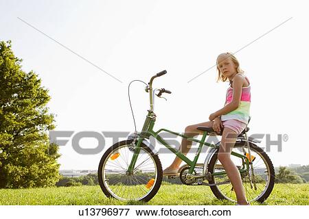 Girl sitting on bicycle in grass View Large Photo Image Stock Photo - Girl sitting on bicycle in grass. Fotosearch