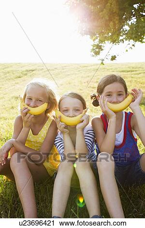 Stock Image - Girls holding bananas over mouths. Fotosearch