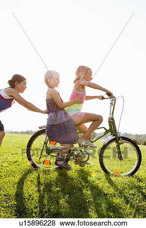Girls playing with bicycle in grass View Large Photo Image Stock Photo - Girls playing with bicycle in grass. Fotosearch
