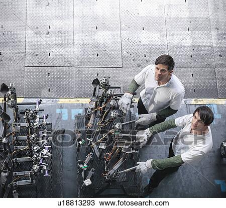 Stock Image - High angle portrait of engineers inspecting press parts in car factory. Fotosearch