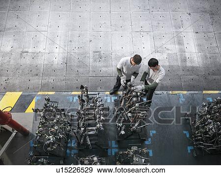 Stock Photo - High angle view of engineers inspecting press parts in car factory. Fotosearch