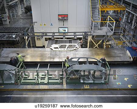 High angle view of workers handling car parts as they come out of press in car factory View Large Photo Image Stock Photo - High angle view of workers handling car parts as they come out of press in car factory. Fotosearch