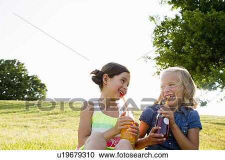 Stock Image - Laughing girls drinking juice outdoors. Fotosearch