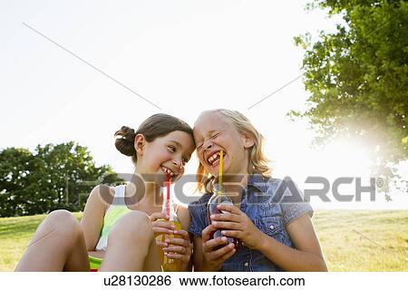 Laughing girls drinking juice outdoors View Large Photo Image Stock Photograph - Laughing girls drinking juice outdoors. Fotosearch