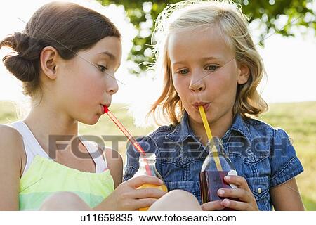 Stock Photography - Laughing girls drinking juice outdoors. Fotosearch