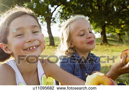 Stock Image - Laughing girls eating apples outdoors. Fotosearch