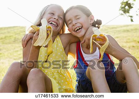 Laughing girls eating bananas outdoors View Large Photo Image Stock Image - Laughing girls eating bananas outdoors. Fotosearch