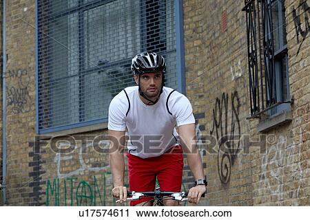 Stock Image - Man bicycling on city street. Fotosearch