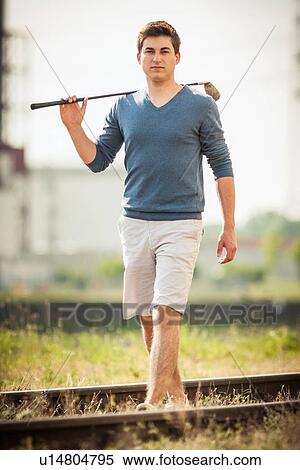 Stock Photography - Man carrying golf club on tracks. Fotosearch