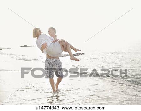 Man carrying wife in waves on beach View Large Photo Image Stock Image - Man carrying wife in waves on beach. Fotosearch