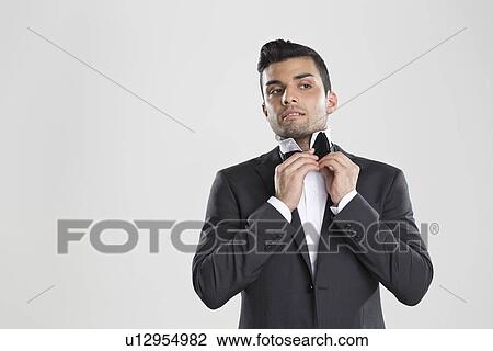 Stock Image - Man in tuxedo adjusting his bow tie. Fotosearch