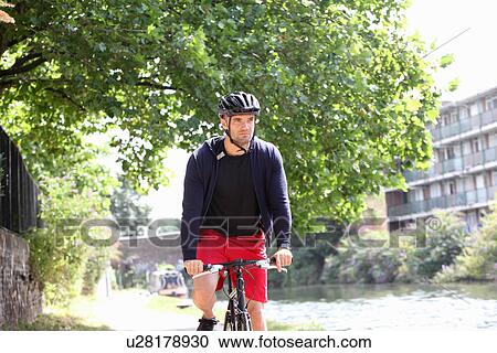 Man riding bicycle by urban river View Large Photo Image Stock Image - Man riding bicycle by urban river. Fotosearch