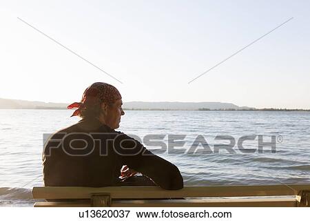 Stock Photo - Man sitting on bench at beach. Fotosearch