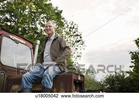Stock Image - Man sitting on vintage tractor outdoors. Fotosearch