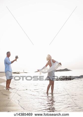 Stock Photo - Man taking pictures of wife on beach. Fotosearch