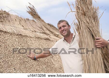 Stock Photograph - Man working on straw roof. Fotosearch