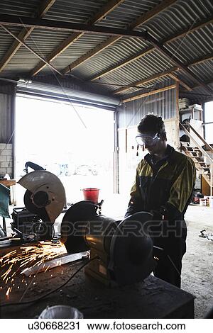 Stock Image - Metal worker using grinder in shop. Fotosearch
