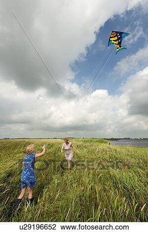 Stock Image - Mother and daughter flying kite in field. Fotosearch