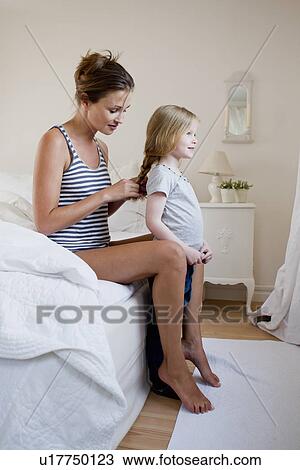 Stock Image - Mother braiding daughters hair. Fotosearch